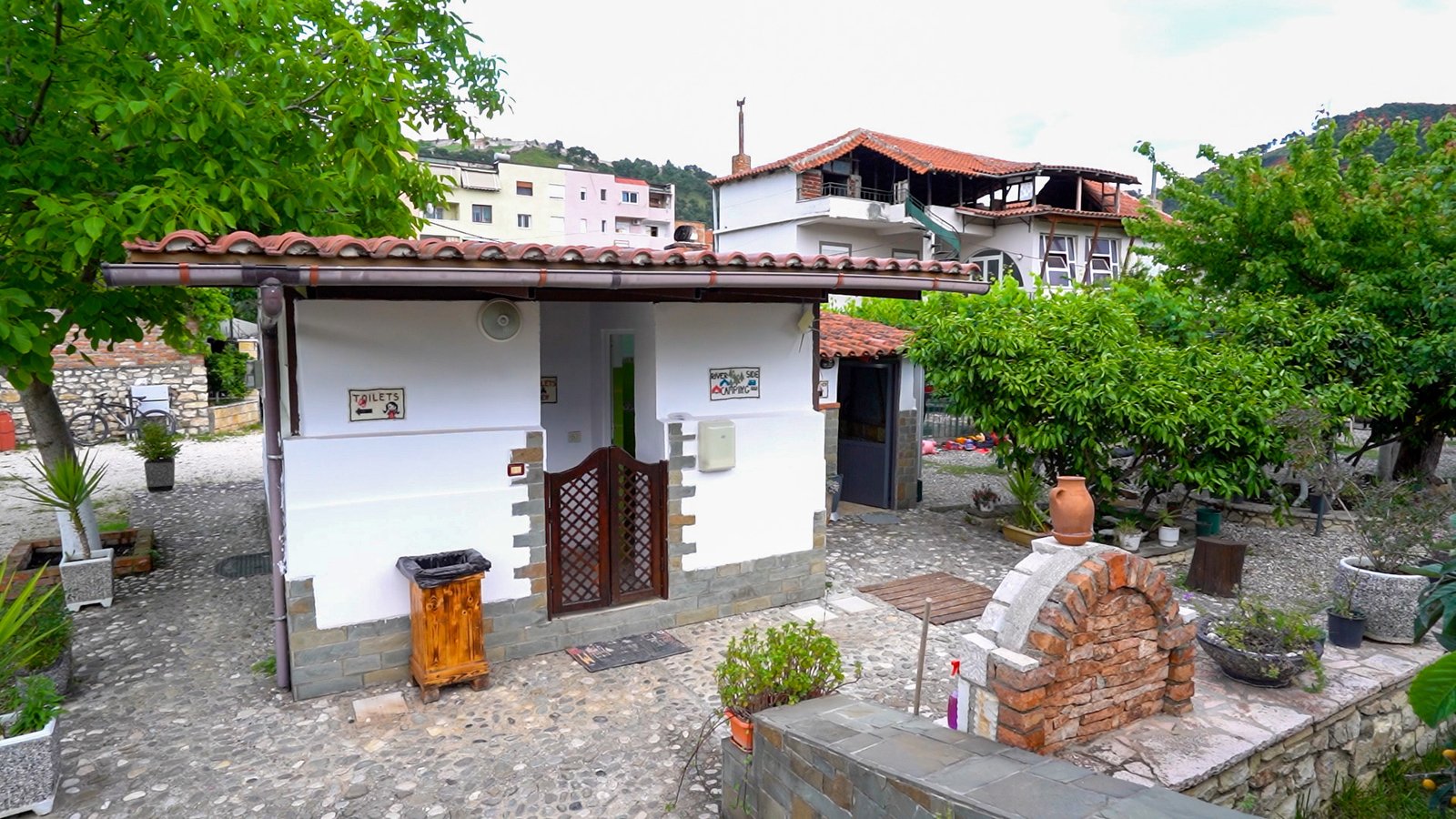 Modern brick building at Riverside Camping Berat housing toilets, hot‑water showers, and a shared kitchen, nestled among lush greenery.